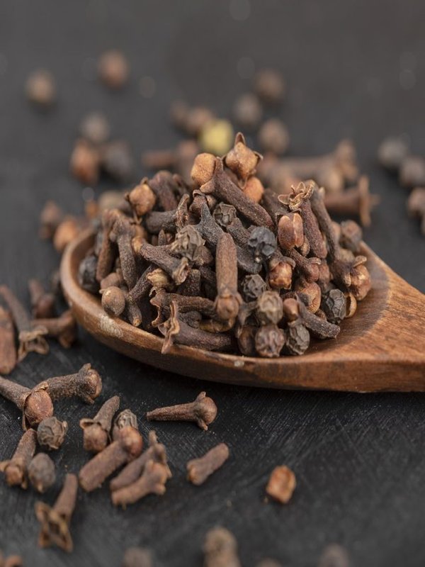 Pile of dried natural cloves with wooden spoon on black surface