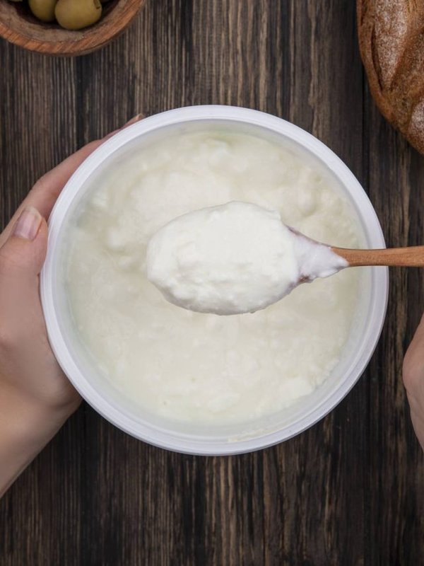 top view woman eating yogurt in bowl with wooden spoon olives and black bread on wooden background