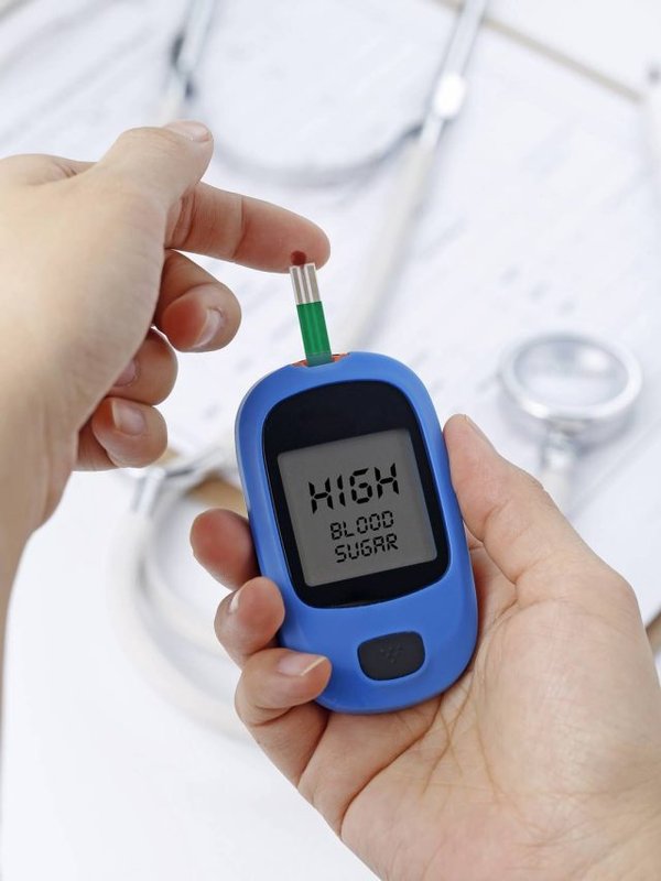 Hand holding a blood glucose meter measuring blood sugar, the background is a stethoscope and chart file