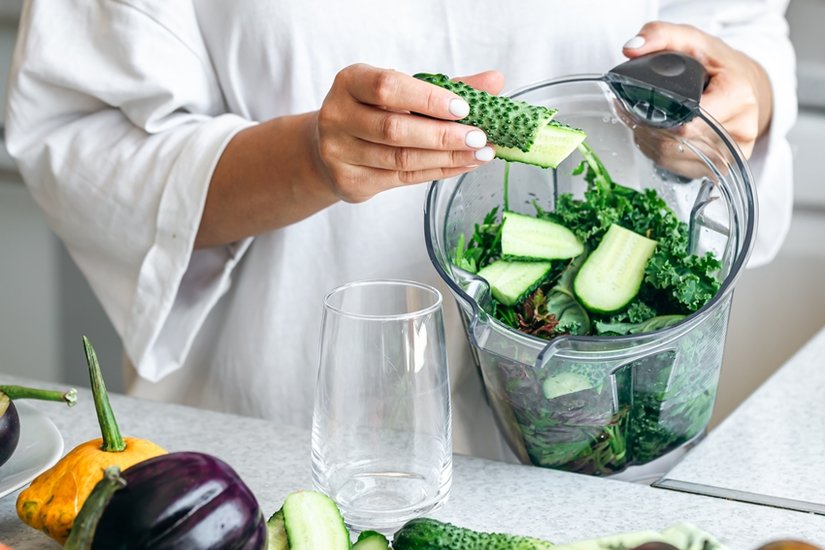 A woman with blender chopping cucumber for smoothie at home.