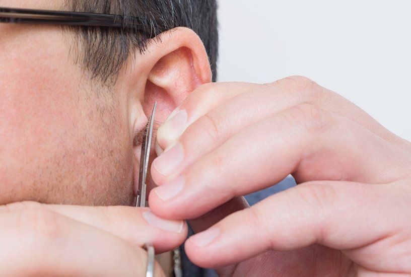 Man removes or cuts his unwanted hair in ears with small scissors at home.