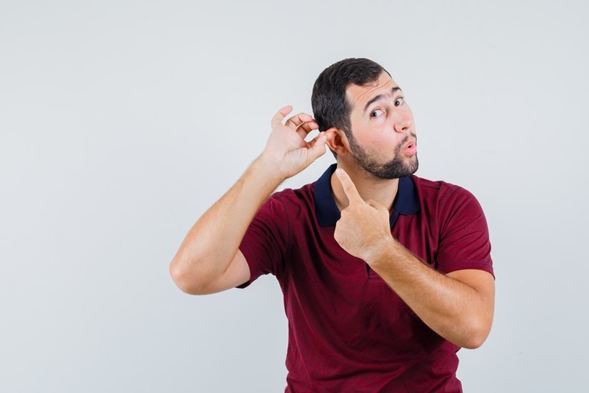 Young male pointing at his ear in red t-shirt and looking focused. front view.