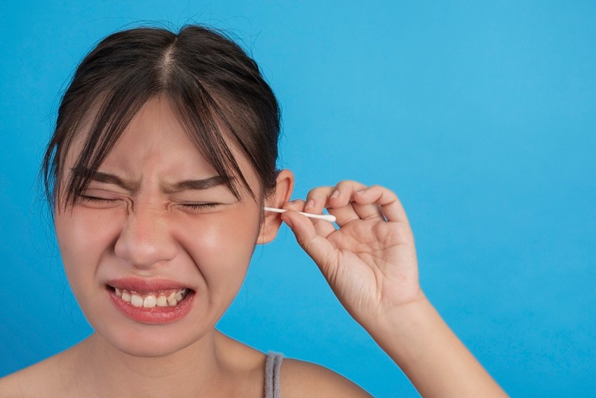 Young girl is ear picking with cotton swab on blue background