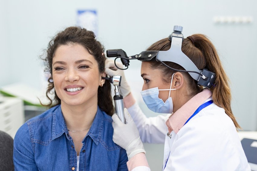 Hearing exam. Otolaryngologist doctor checking woman's ear using otoscope or auriscope at medical clinic.