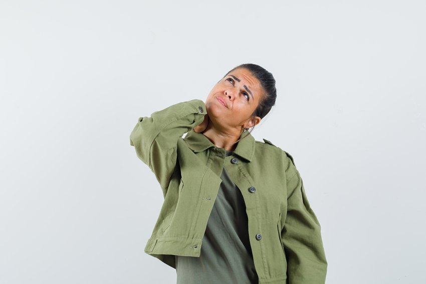 woman holding hand on neck in jacket, t-shirt and looking hesitant. front view.