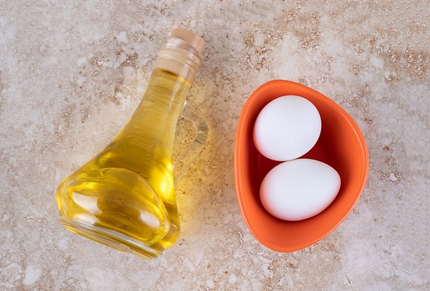 Two fresh white chicken eggs with a glass bottle of oil