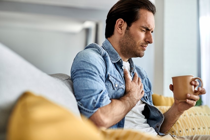 Young man having a chest pain while drinking tea at home.